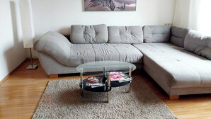 A modern living room with a grey sectional sofa, a glass coffee table with magazines, and a framed picture of a beach scene on the wall. - Guesthouse Graz Central for 9 People (Graz)