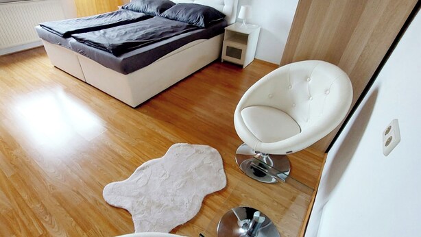 A modern bedroom with a large bed, a white armchair, a small table, and a unique rug. - Guesthouse Graz Central for 9 People (Graz)