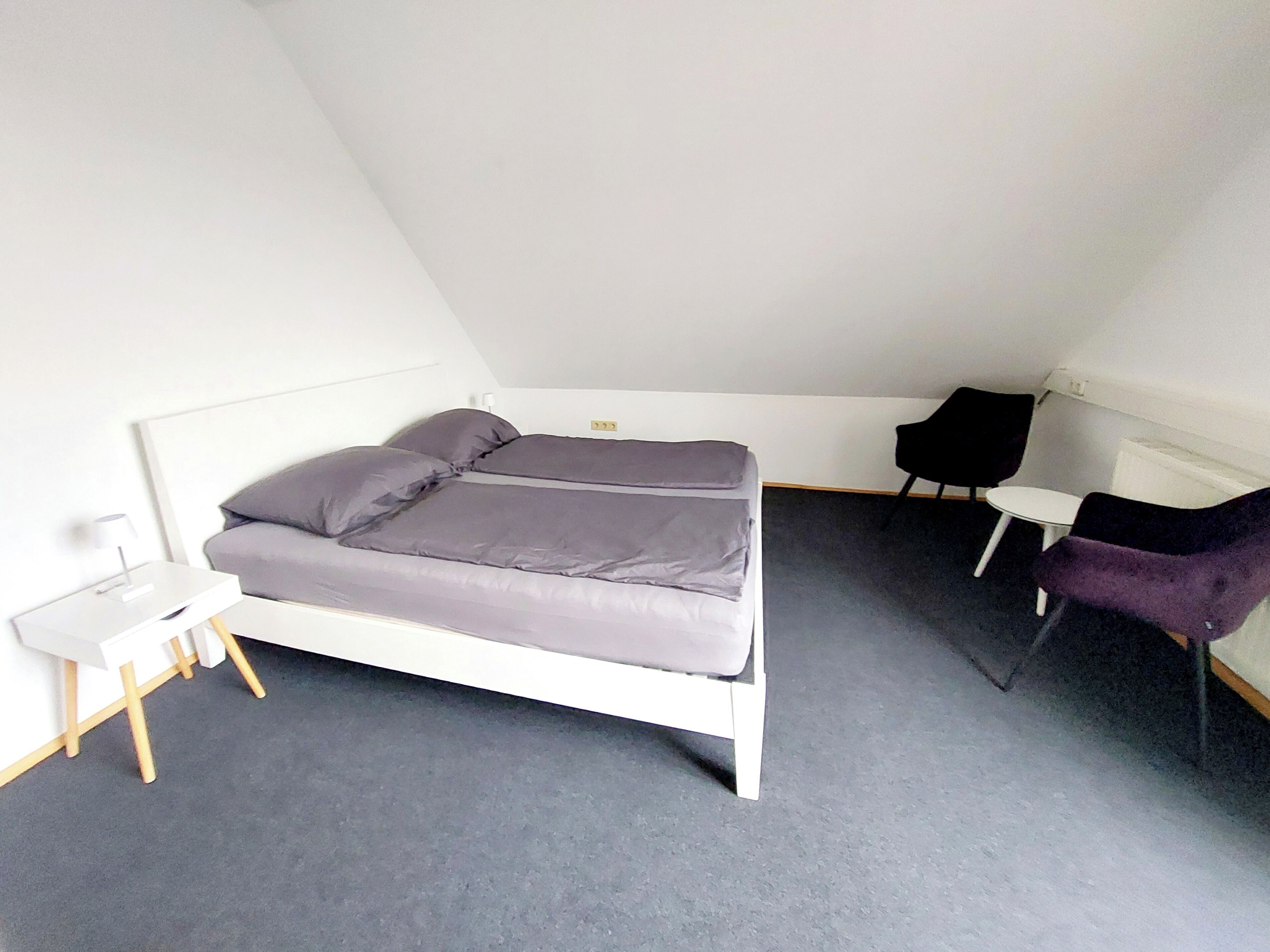 Ein Zimmer mit einem Bett, einem kleinen Tisch, zwei Stühlen und einer weißen Wand.