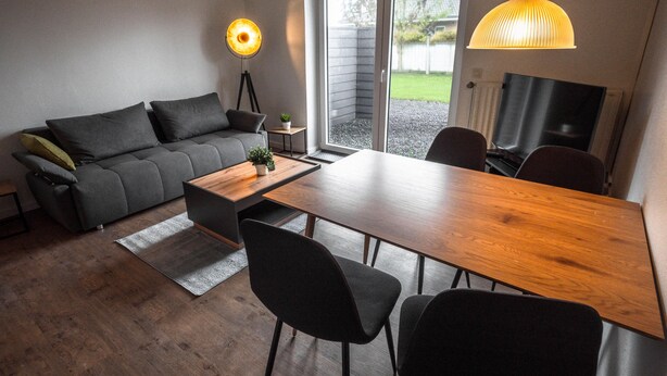A modern living room with a sofa, dining table, chairs, and a TV. - Cozy vacation home Deichkoje 2 in Dagebüll with terrace and garden (Dagebüll)