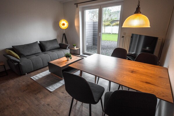 A modern living room with a sofa, dining table, chairs, and a TV.