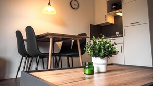 A modern kitchen with a wooden table, black chairs, a potted plant, and a clock on the wall. - Cozy vacation home Deichkoje 2 in Dagebüll with terrace and garden (Dagebüll)