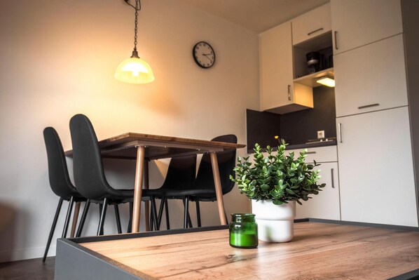 A modern kitchen with a wooden table, black chairs, a potted plant, and a clock on the wall. - Cozy vacation home Deichkoje 2 in Dagebüll with terrace and garden (Dagebüll)