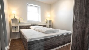 Ein Schlafzimmer mit einem Bett, Nachttischlampen, einem Fenster und Holzboden.