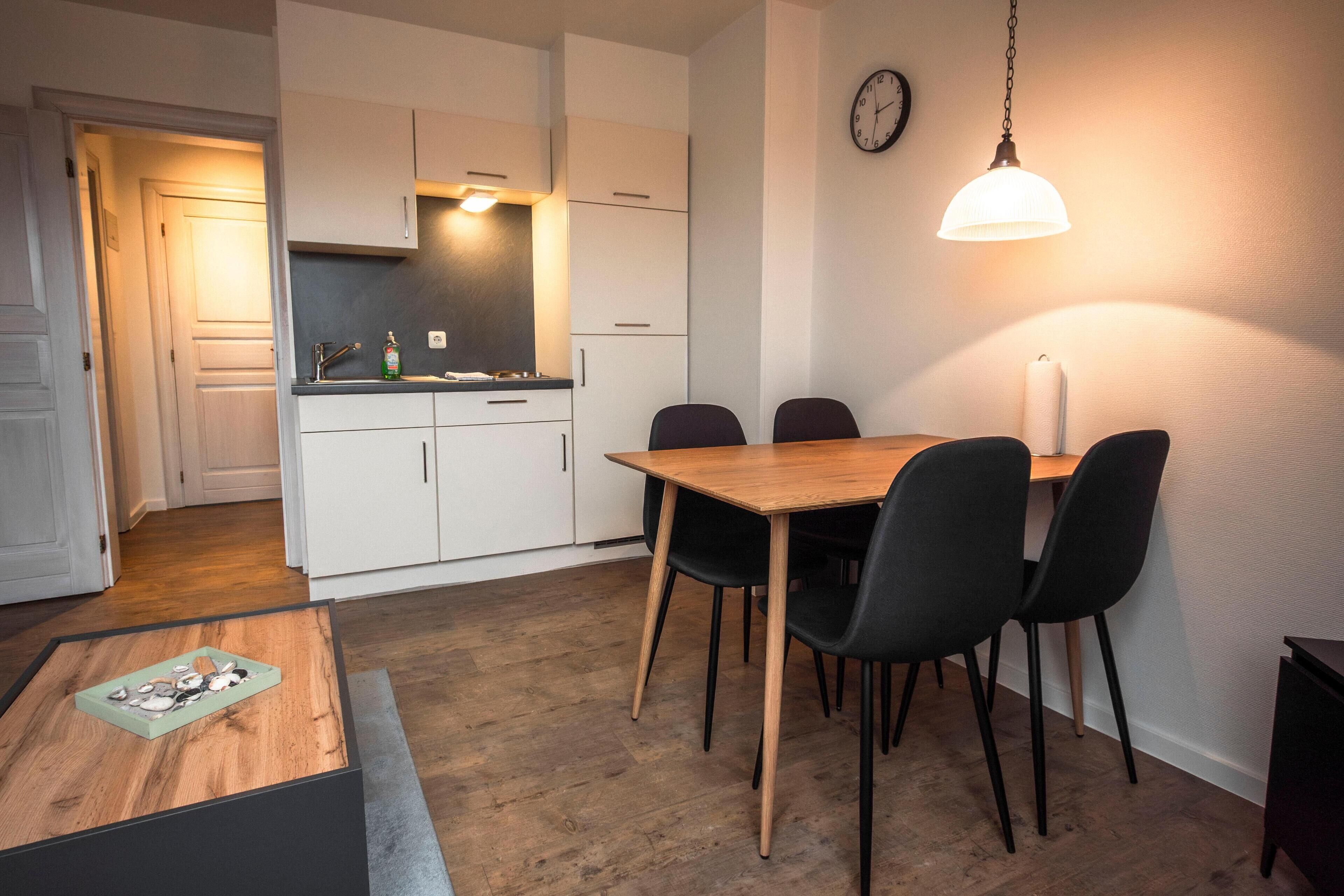 Une cuisine moderne avec des meubles blancs, une table à manger en bois et des chaises noires.