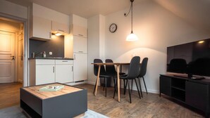 Une cuisine moderne avec des meubles blancs, une table à manger avec des chaises, une table basse et un téléviseur posé sur un meuble.