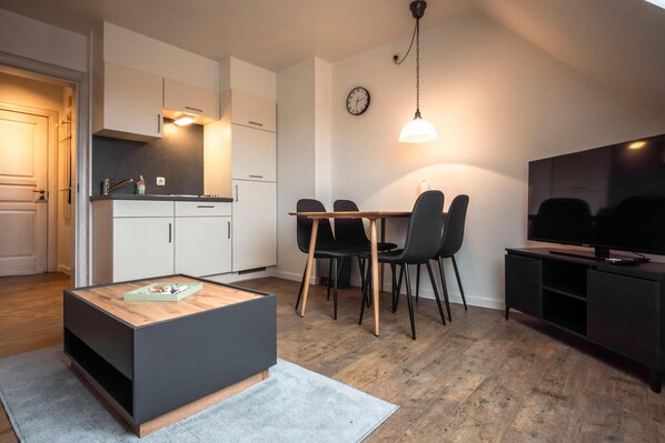 A modern kitchen with white cabinets, a dining table with chairs, a coffee table, and a TV on a cabinet.