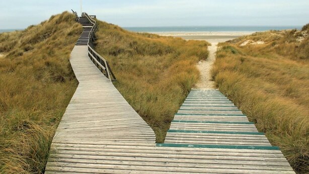 A wooden boardwalk leading to a beach, surrounded by dunes. - Apartment Deichkoje 4 in Dagebüll, featuring modern amenities and a location near the North Sea (Dagebüll)