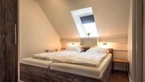 A bedroom with a sloped ceiling, a skylight, a bed with white bedding, a small bedside table, and a radiator. - Apartment Deichkoje 4 in Dagebüll, featuring modern amenities and a location near the North Sea (Dagebüll)