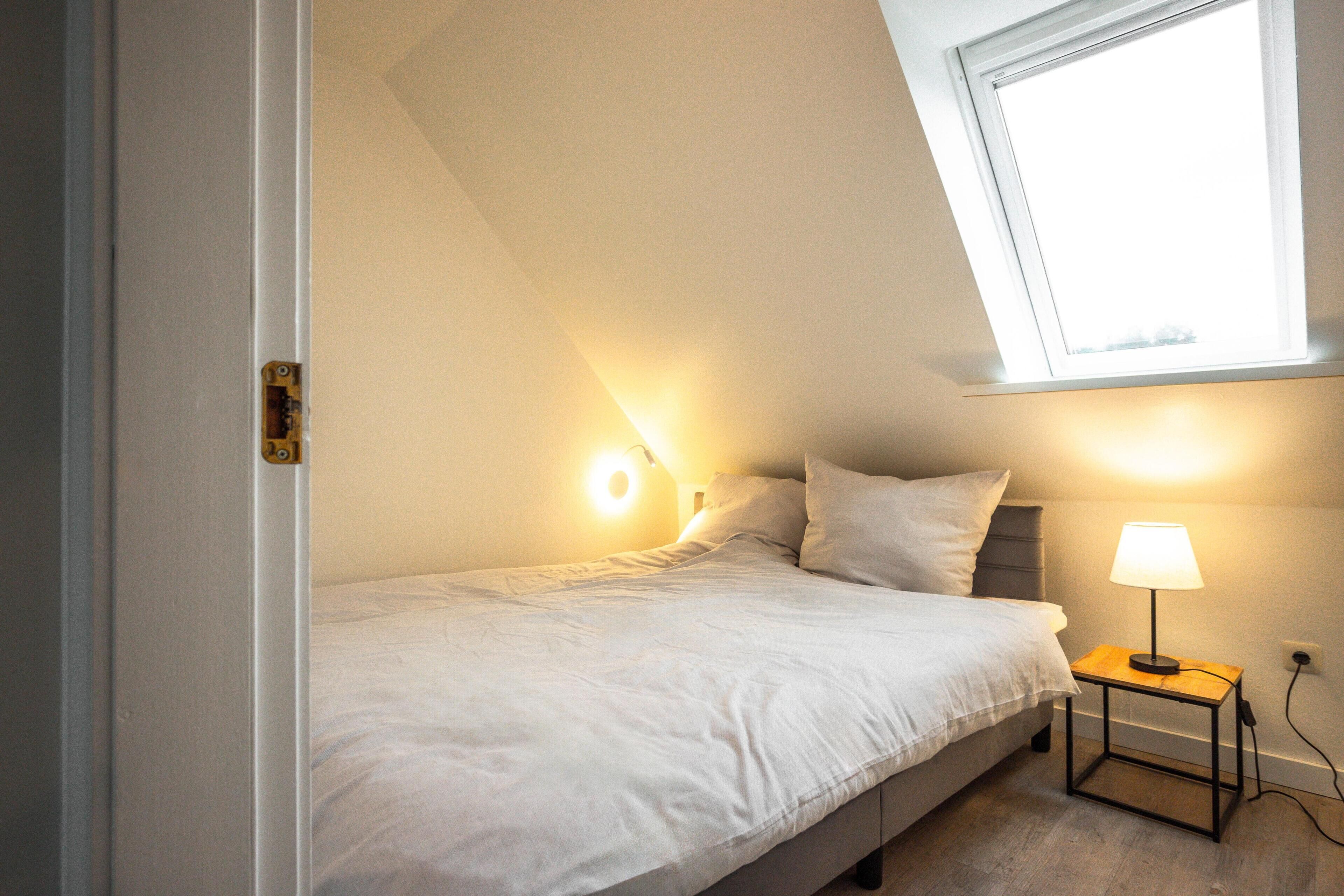 Ein Schlafzimmer mit einem Einzelbett, einem Nachttisch mit Lampe und einem Oberlicht.