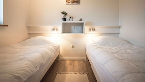 Ein Schlafzimmer mit zwei Einzelbetten, einem Nachttisch mit Uhr und Pflanze, einem Regal mit einem Bild und einem kleinen Teppich auf dem Boden.