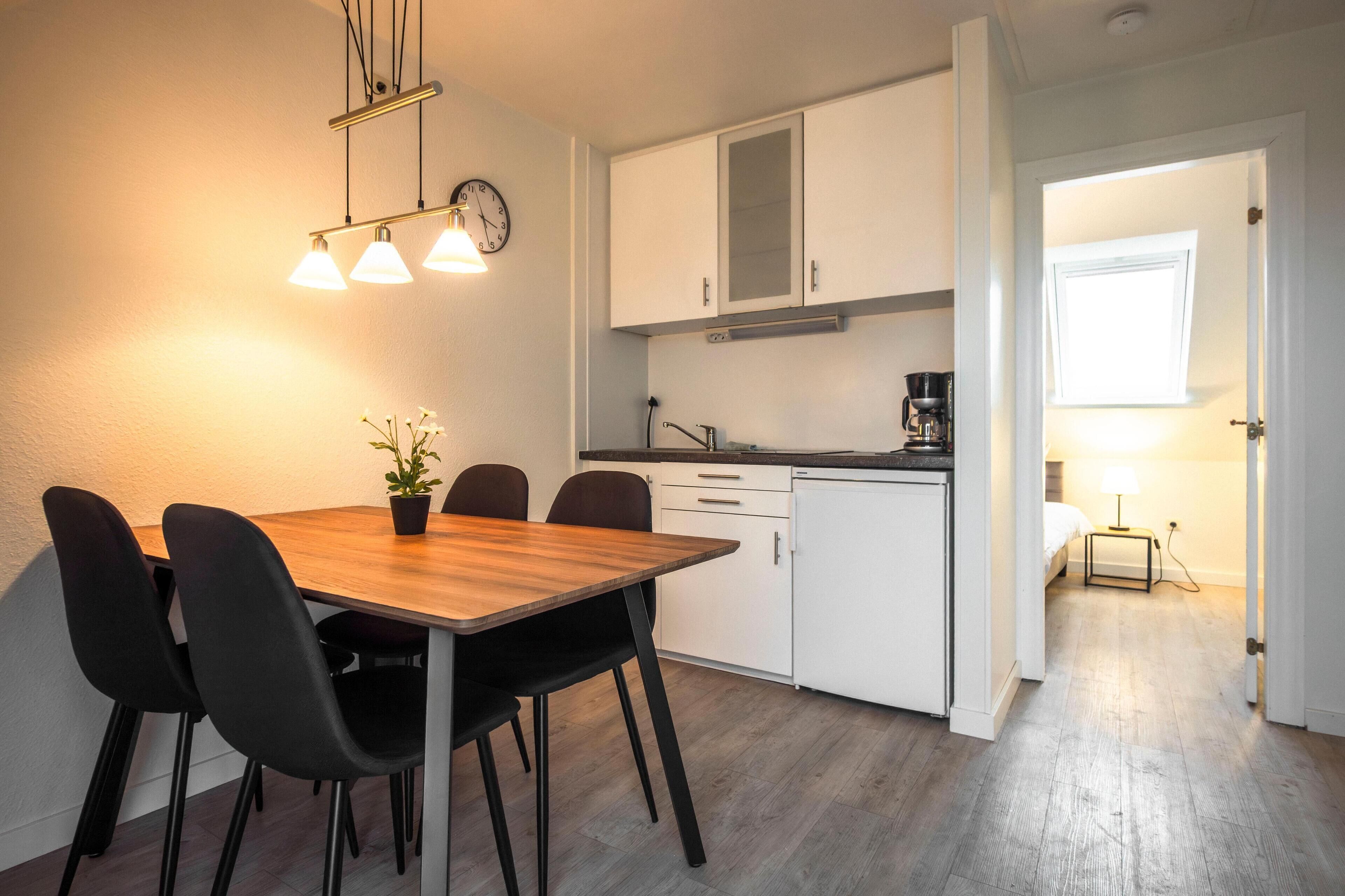 Een moderne keuken met witte kasten, een houten eettafel en zwarte stoelen.