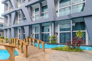 Ein modernes Hotel mit mehreren Stockwerken, großen Fenstern und einem Poolbereich mit einer Holzbrücke.
