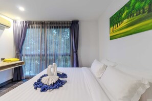 Ein Hotelzimmer mit einem ordentlich bezogenen Bett, einem Bild von einem von Bäumen gesäumten Pfad an der Wand und einem Fenster mit Vorhängen.