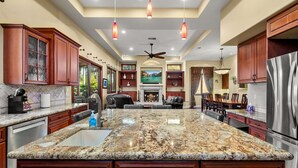 A spacious kitchen with granite countertops, wooden cabinets, and a central island. - Tuscan Sands by Coastline Vacation Rentals (San Diego)