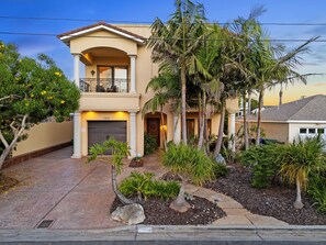 A two-story house with a balcony, a garage, and a well-maintained garden with palm trees and shrubs. - Tuscan Sands by Coastline Vacation Rentals (San Diego)