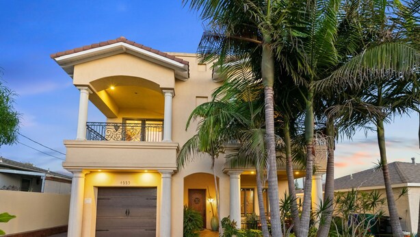 A two-story house with a balcony, a garage, and a well-maintained garden with palm trees. - Tuscan Sands by Coastline Vacation Rentals (San Diego)