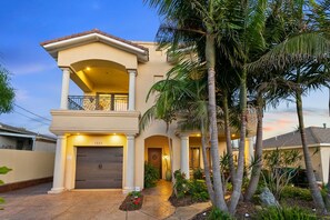 Una casa a due piani con un balcone, un garage e un giardino curato con palme.