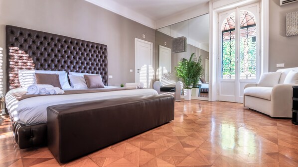 A spacious bedroom with a large bed, a seating area, and a view of the outdoors.