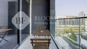 A balcony with a table and benches, large windows, and a view of the cityscape. - 520 Bloomfields 1BR Azizi Riviera (Dubai)