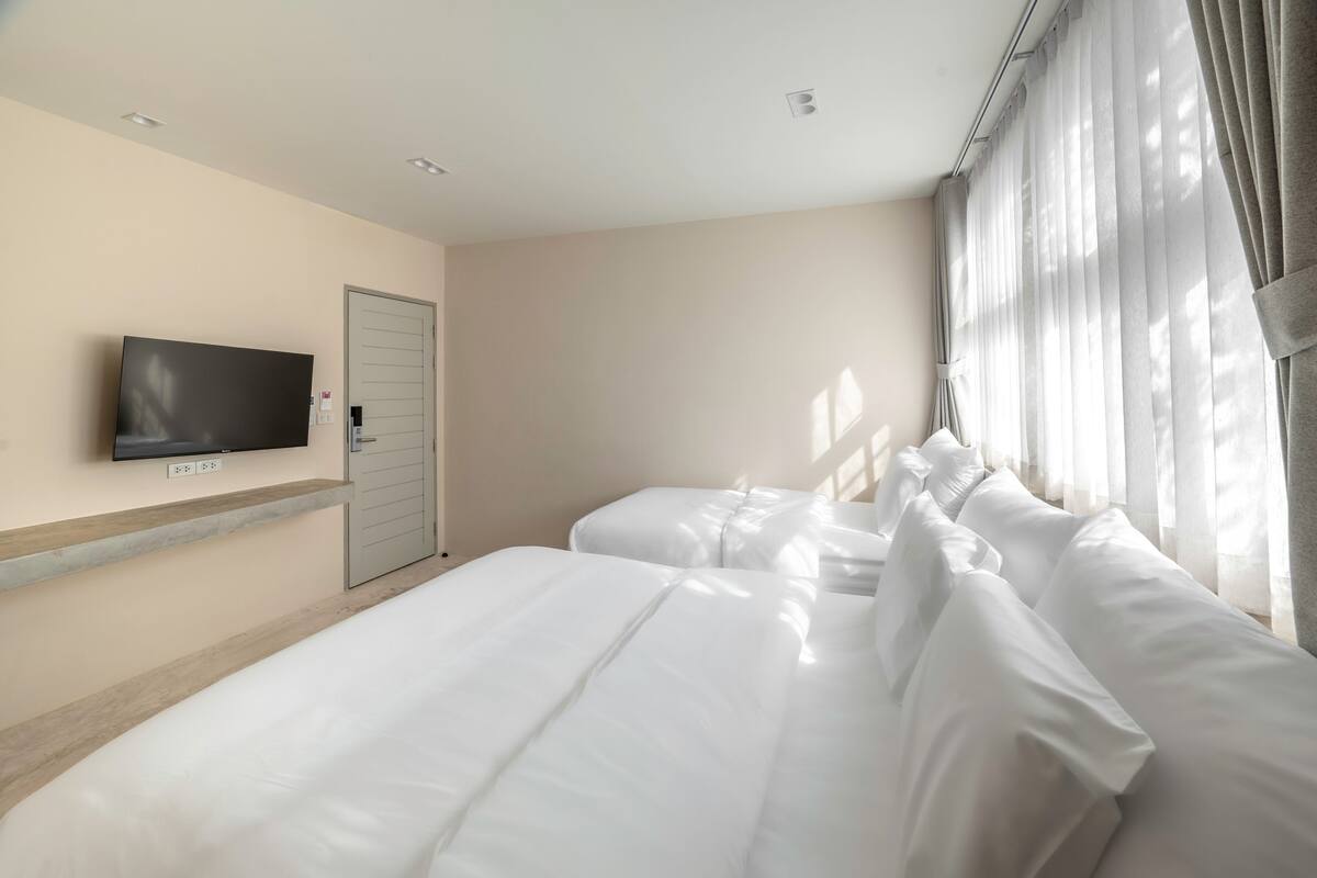 A hotel room with a large bed, a flat-screen TV mounted on the wall, and a window with sheer curtains.