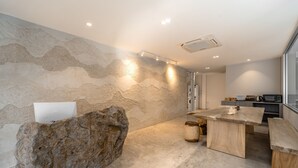 A modern kitchen with a large rock centerpiece, a wooden dining table, and a stone wall. - Siam Escape (Bangkok)