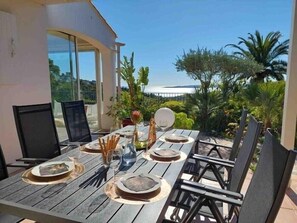 Ein Essbereich im Freien mit einem Tisch für vier Personen, umgeben von Stühlen, und im Hintergrund ein schöner Blick auf das Meer und die Hügel.