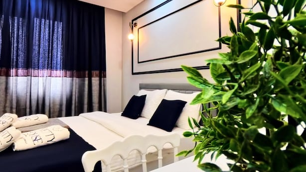 Un dormitorio moderno con una cama, mesitas de noche, una planta y un cabecero con iluminación integrada.