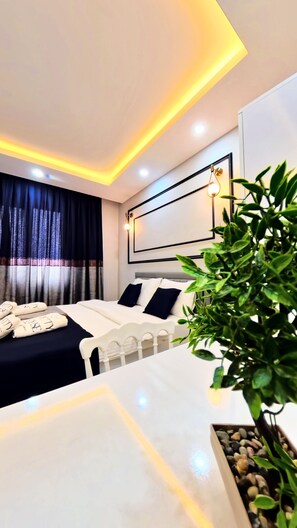 A modern bedroom with a bed, bedside tables, a plant, and a headboard with built-in lighting. - Pretty House  (Pamukkale)