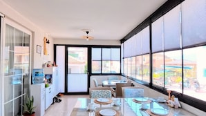 Un comedor amplio con una mesa larga, sillas de mimbre y ventanas grandes que ofrecen vista a la calle.
