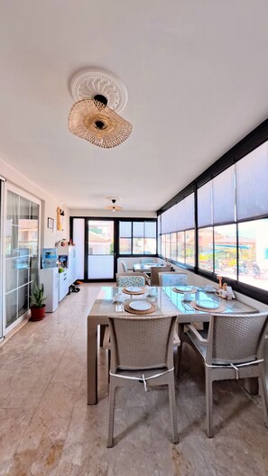 A spacious dining area with a long table, wicker chairs, and large windows offering a view of the street.