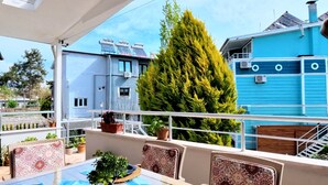 Un área de comedor al aire libre con una mesa preparada para cuatro, rodeada de sillas, y vistas a una zona residencial con casas y un árbol grande.