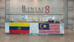 Un comptoir d’accueil orné des drapeaux de la Colombie et de la Malaisie, et une enseigne indiquant « Binjai 8 Premium Soho ».