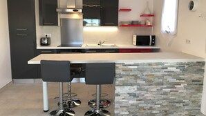 A modern kitchen with a central island, black cabinets, a stainless steel range hood, a microwave, and a red shelf. - VILLA CARA (Mougins)