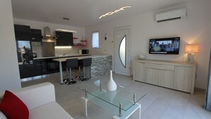A modern kitchen with a dining area, a TV mounted on the wall, and a sofa with a red pillow. - VILLA CARA (Mougins)