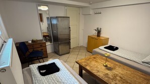 Una habitación compacta con cama, una mesa de madera, un mueble pequeño, un refrigerador y un radiador.