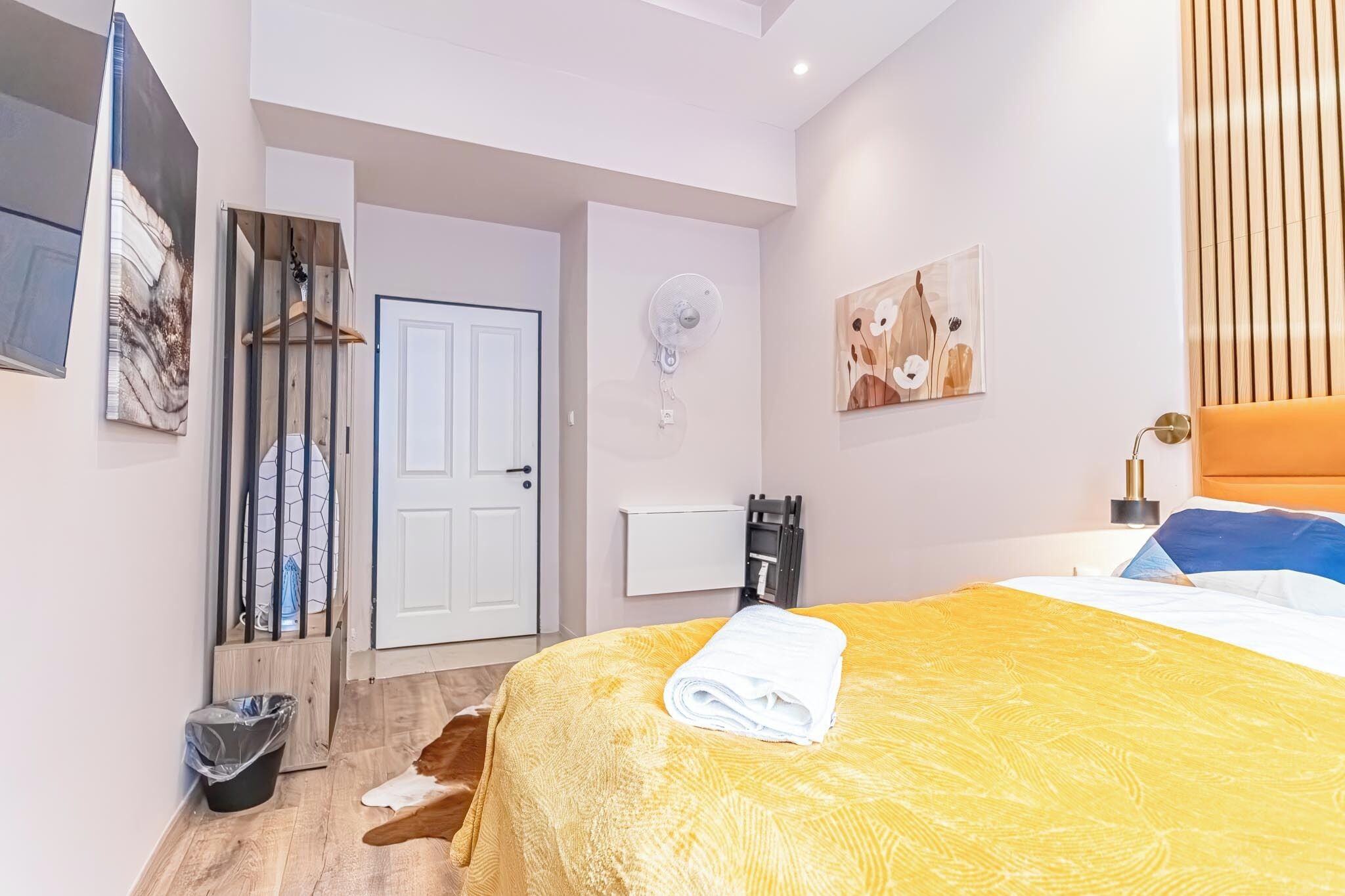 Une chambre d’hôtel avec un lit, une porte blanche, un ventilateur fixé au mur et un tableau.