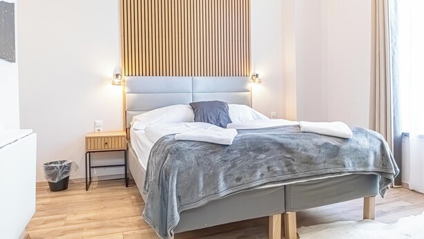 Un dormitorio ordenado con cama, mesita de noche y lámpara fijada a la pared.
