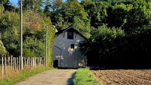 Una strada di campagna che conduce a un edificio bianco con tetto scuro, circondato da alberi e da una recinzione.