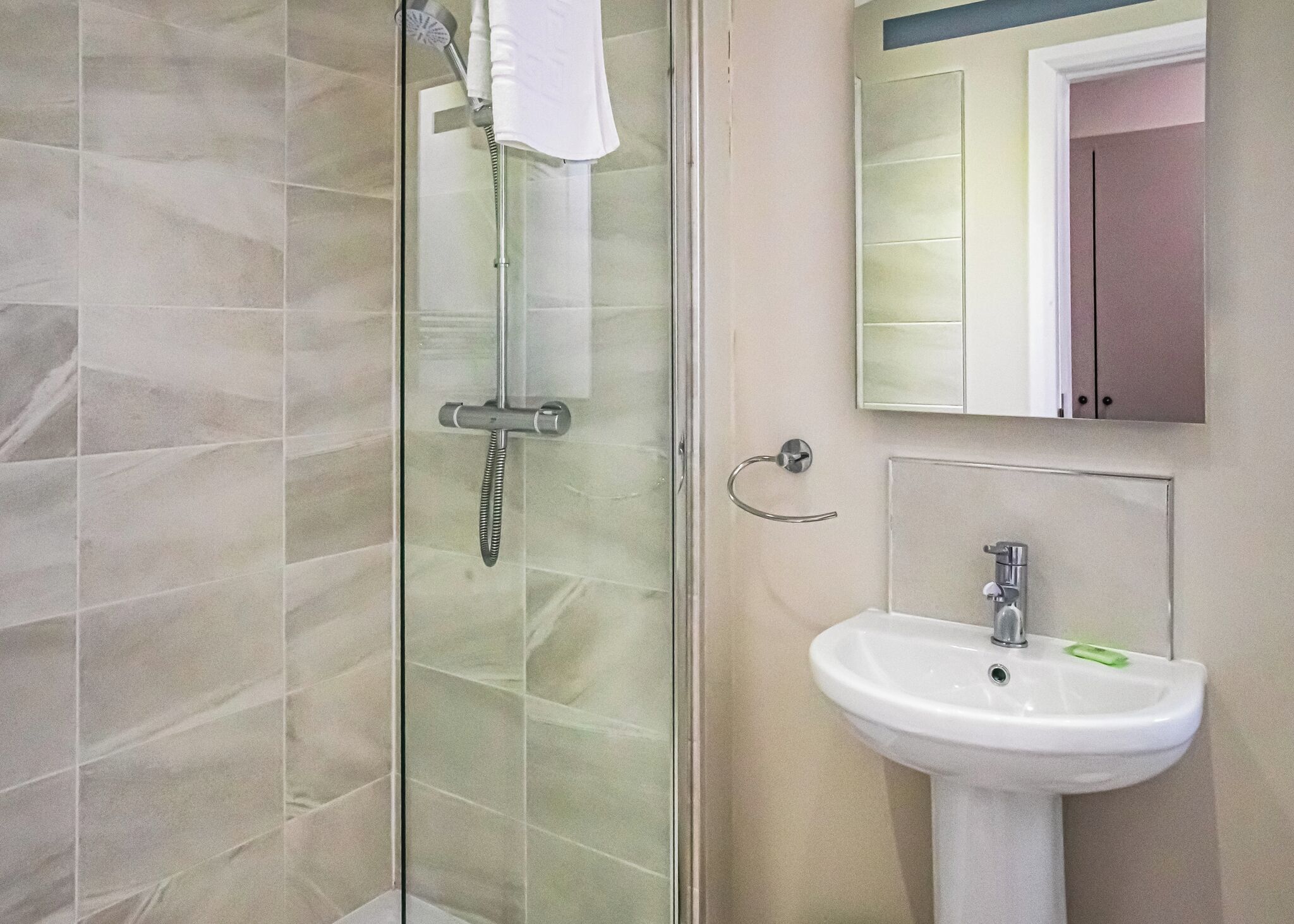 Een badkamer met een douchecabine van glas, een witte wastafel en een spiegel boven de wastafel.