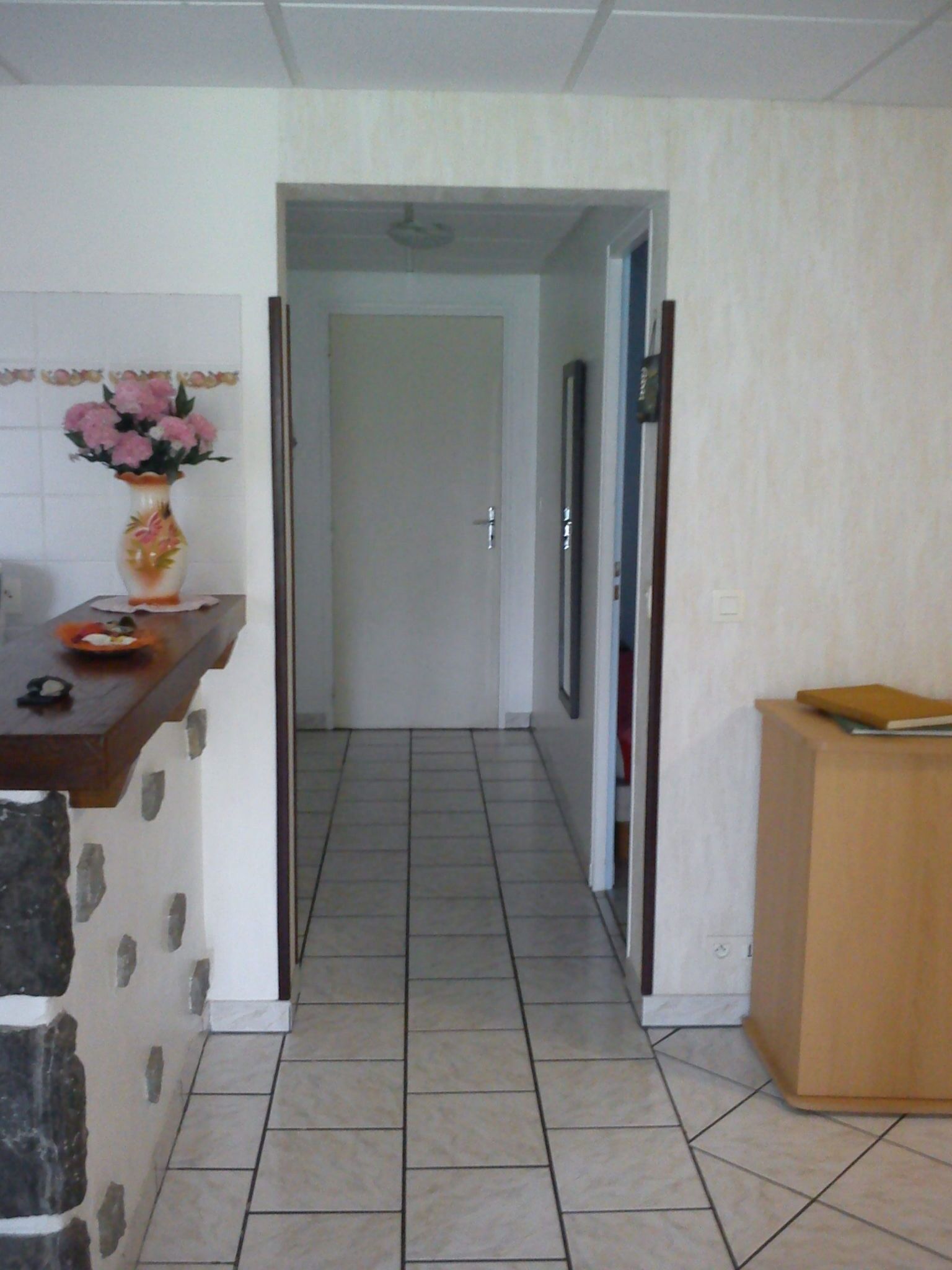 A hallway with a tiled floor, a wooden counter with a vase of flowers, and a wooden cabinet.