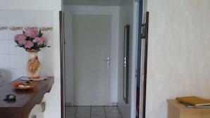 A hallway with a tiled floor, a wooden counter with a vase of flowers, and a wooden cabinet. - Rental Apartment Type T2 Curistes ou Vacanciers (Halsou)