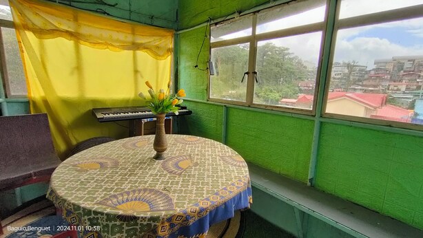 Une pièce avec un mur vert, une table ronde recouverte d’une nappe à motifs, un clavier et un vase rempli de fleurs.