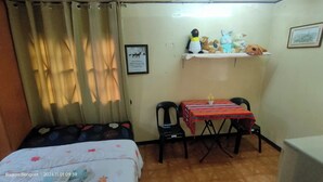 Une petite pièce comprenant un lit, un bureau avec une chaise, une étagère avec des peluches et un tableau encadré accroché au mur.