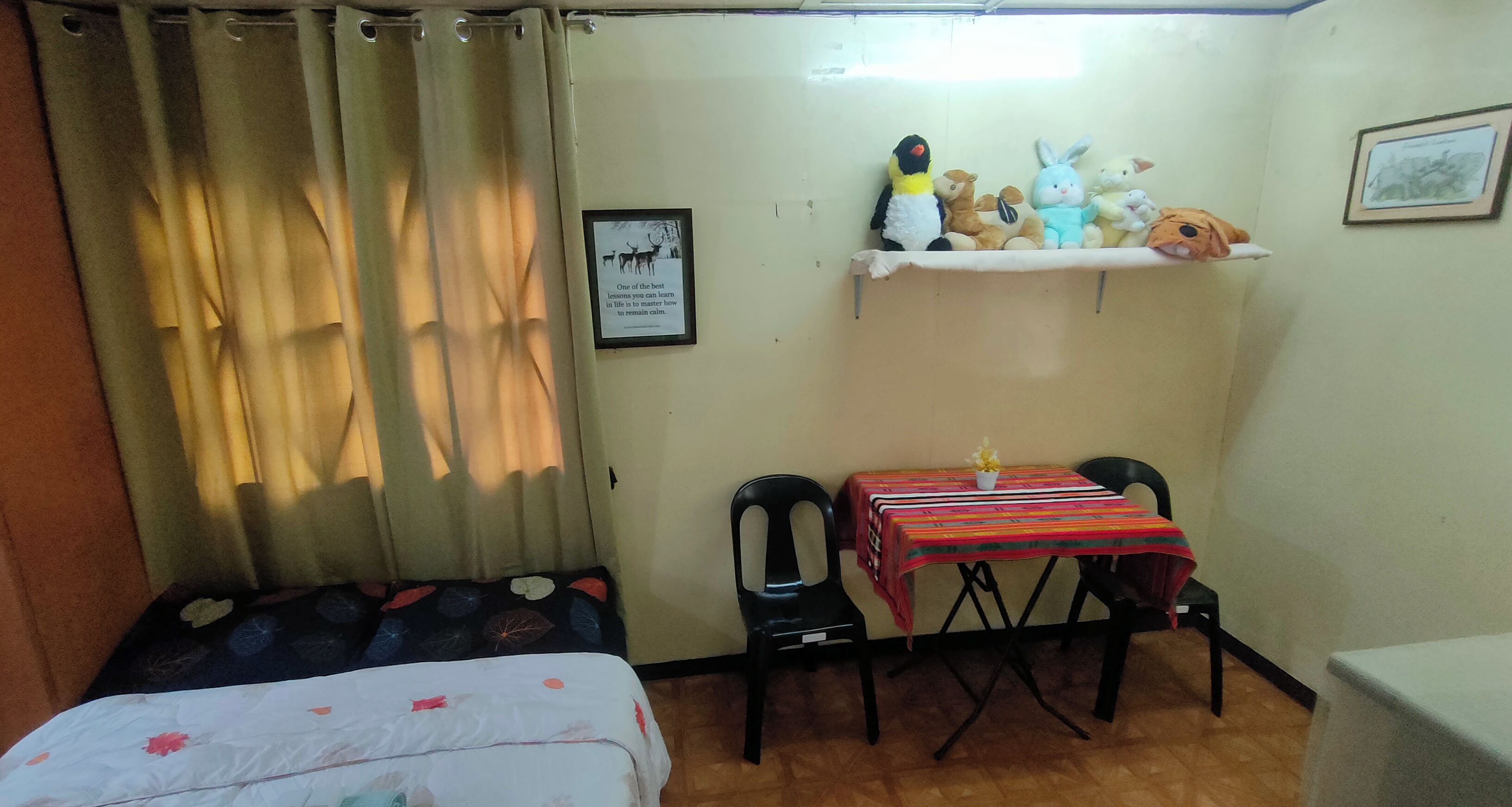 A small room with a bed, a desk with a chair, a shelf with stuffed toys, and a framed picture on the wall.