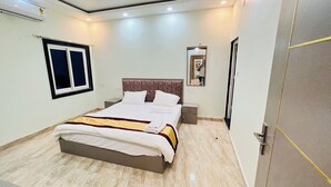 A bedroom with a bed, bedside tables, a wardrobe, a window, and an air conditioning unit. - sandhya paying guest house (Varanasi)
