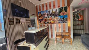 A reception area with a reception desk, a television mounted on the wall, and a large mural depicting a cityscape. - sandhya paying guest house (Varanasi)