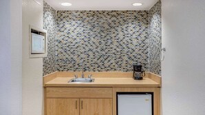 Una cocina compacta con salpicadero de azulejos, un lavamanos, una cafetera y un refrigerador.