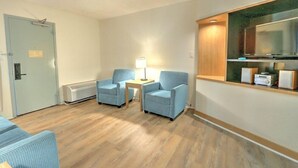 Habitación de hotel con piso de madera, dos sillones azules, una mesita de noche con lámpara, televisor y minibar.