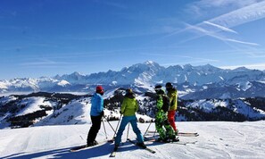 Eine Gruppe von Skifahrern auf einem verschneiten Berghang, im Hintergrund ein freier Blick auf schneebedeckte Gipfel.
